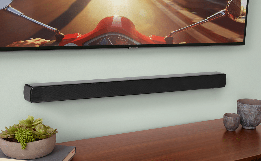 Barra de sonido para televisor JBL Cinema SB170 montada en la pared debajo de un TV sobre un mueble de madera