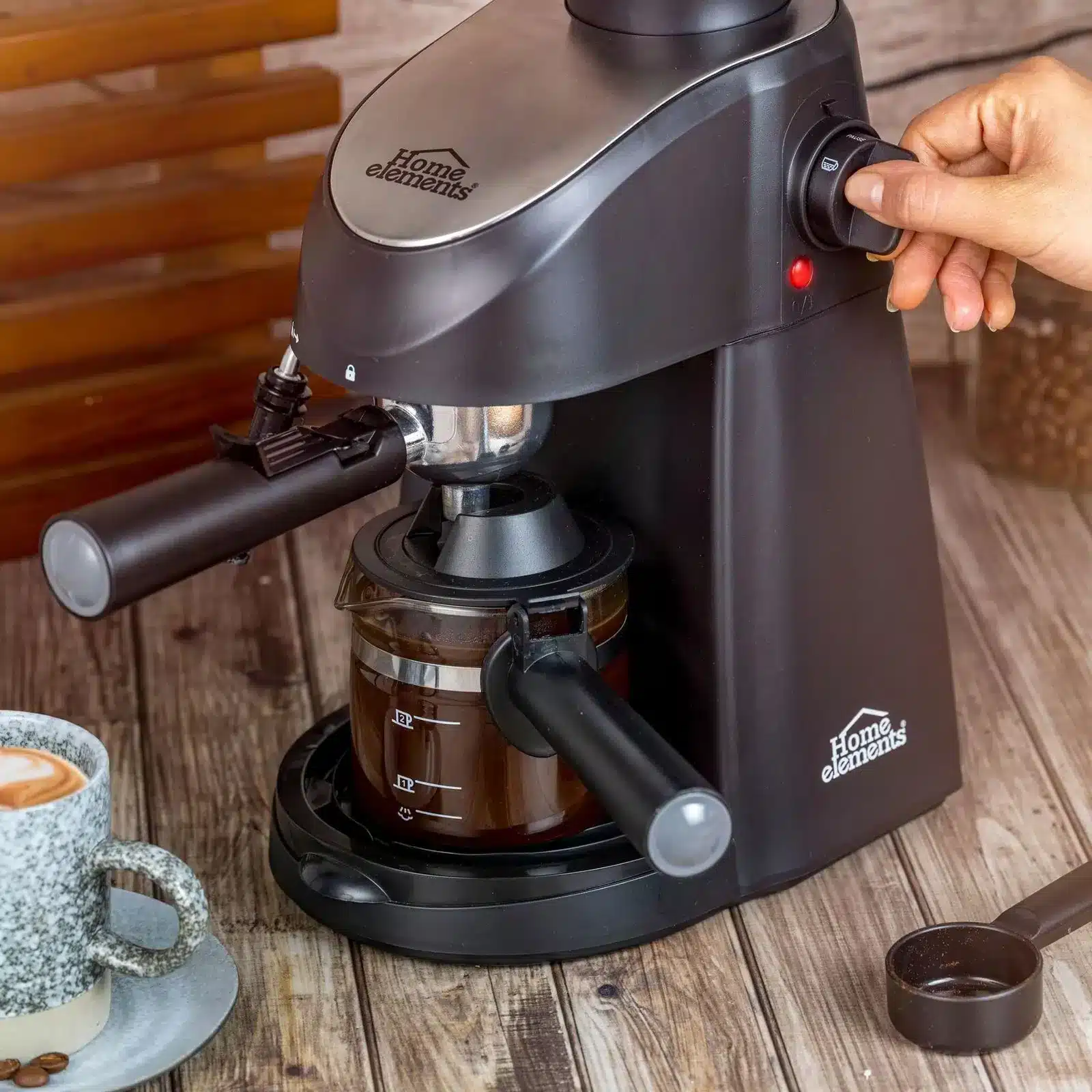 Mano girando la perilla de la cafetera espresso Home Elements HECM-2033N mientras sirve café en jarra de vidrio