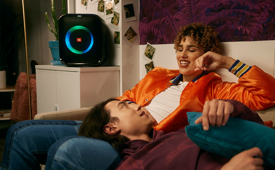 Pareja descansa en el sofá mientras suena el parlante JBL original PartyBox Encore Essential con luz azul