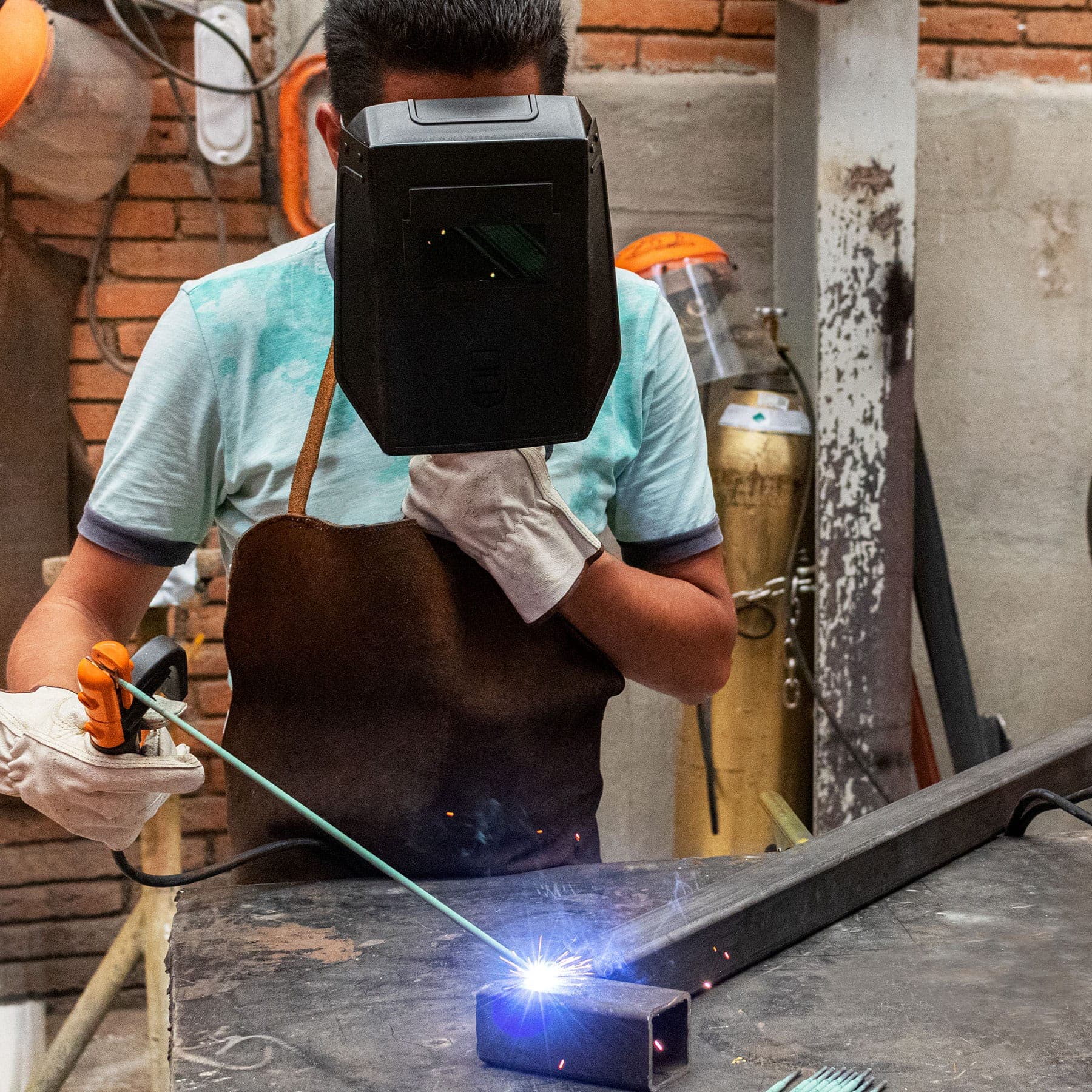 Soldador con careta y guantes uniendo tubo cuadrado de acero con la soldadora inversora 130A Truper y electrodo
